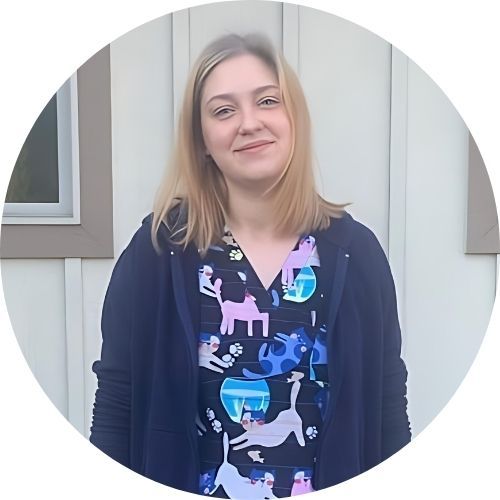 A woman standing in front of a light-colored wall, wearing a colorful shirt with animal patterns and a dark jacket.