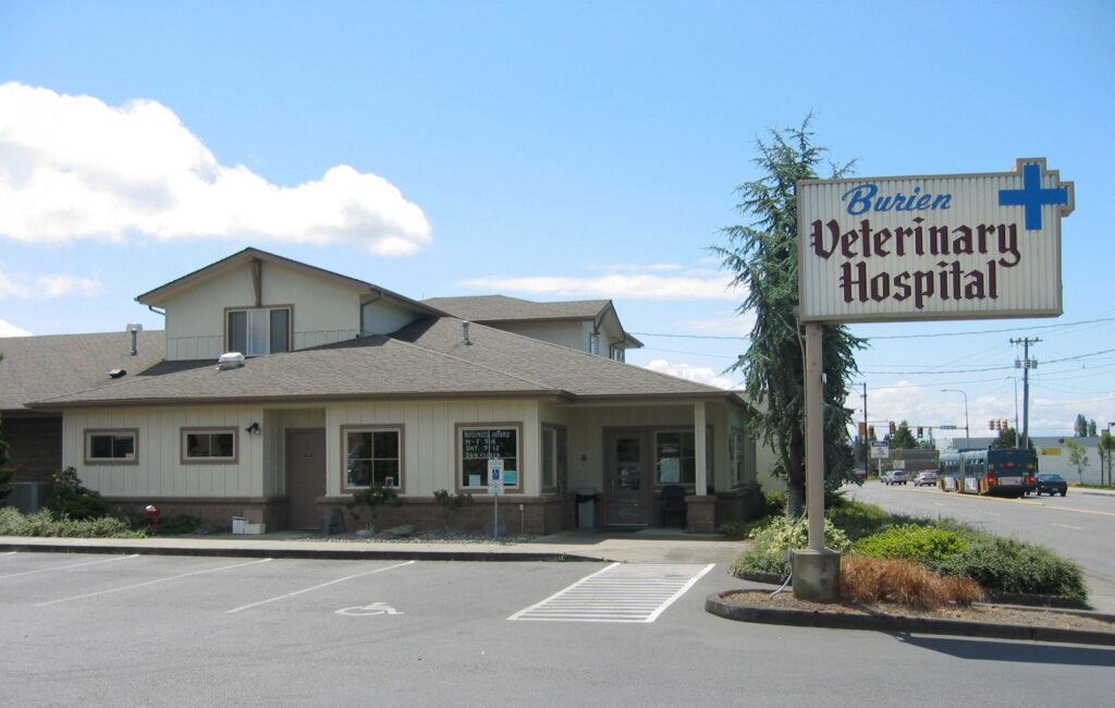 A veterinary hospital building with a sign and parking area, located along a busy street under a partly cloudy sky.